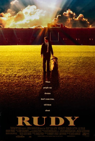
Photographie d’une affiche du film Rudy montrant un jeune homme marchant seul sur un terrain de football éclairé par un coucher de soleil spectaculaire. L’image illustre le thème central du film : la détermination et la poursuite des rêves dans le sport.
