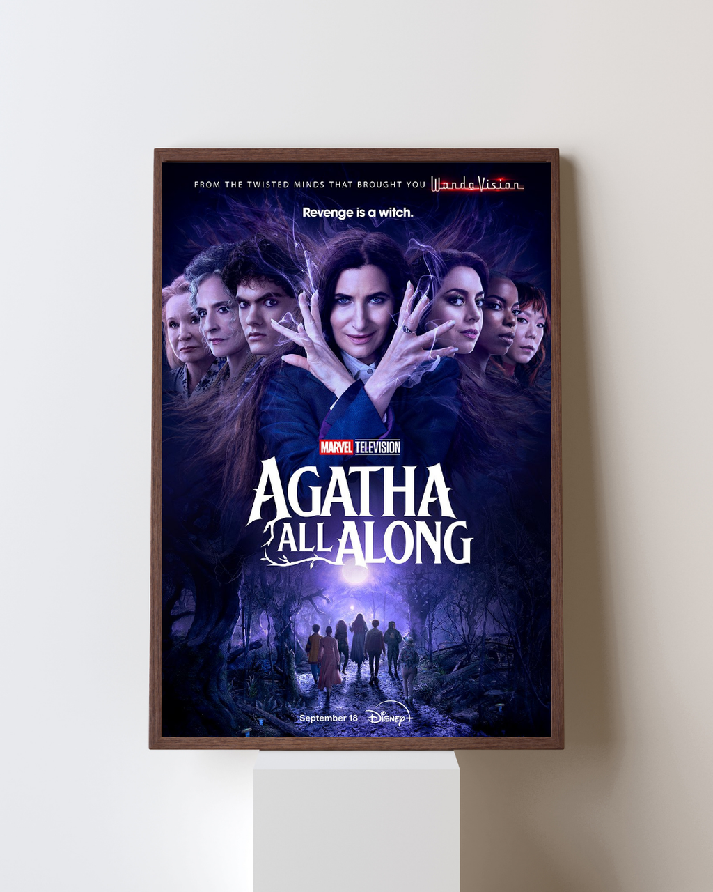 Affiche encadrée de la série Agatha All Along représentant une sorcière au centre avec aura magique et silhouettes dans une forêt sombre, accrochée dans un intérieur moderne, style Marvel fantastique.

