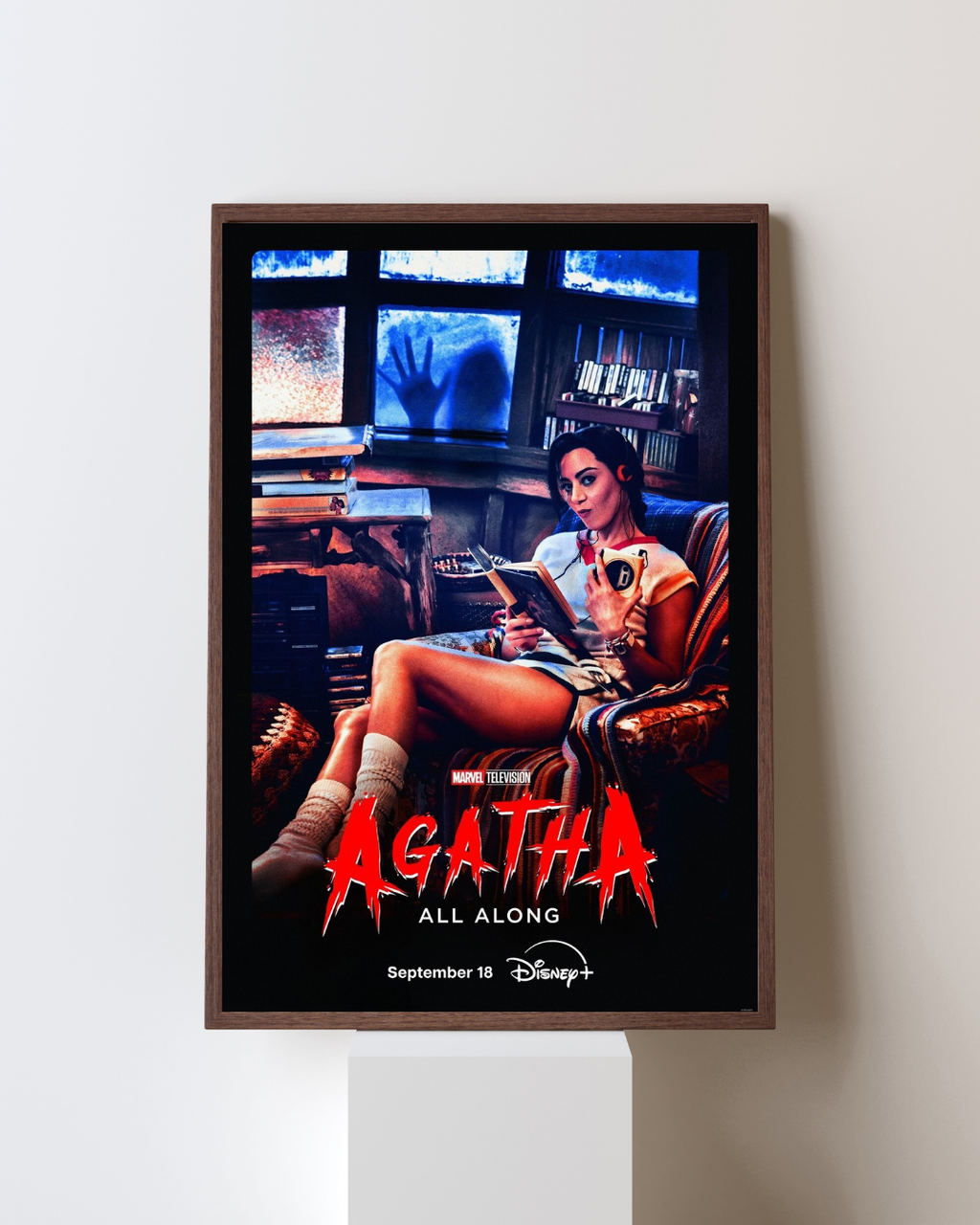 Affiche encadrée de la série Agatha All Along représentant une femme dans une pièce cosy avec une présence inquiétante en arrière-plan, accrochée dans un intérieur moderne, style fantastique Marvel.
