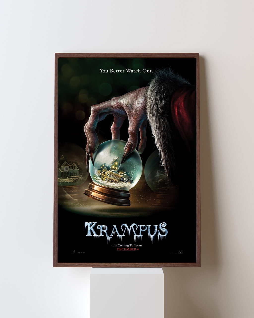 Affiche encadrée du film Krampus représentant une créature tenant une boule à neige avec une scène de maison enneigée, accrochée dans un intérieur moderne, style horreur de Noël.
